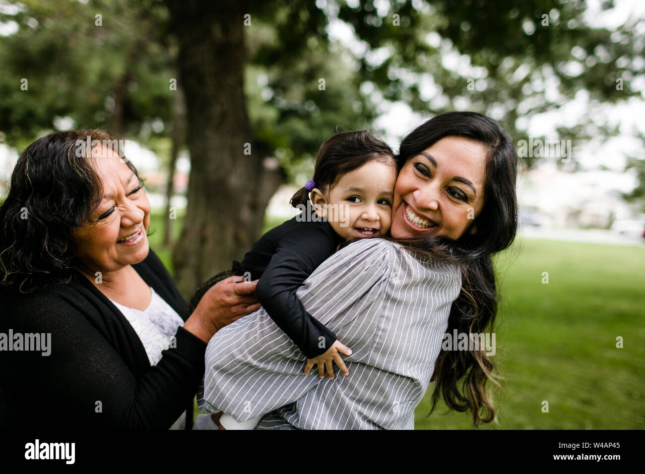 Grandmother, mother & daughter hugging and laughing in park Stock Photo