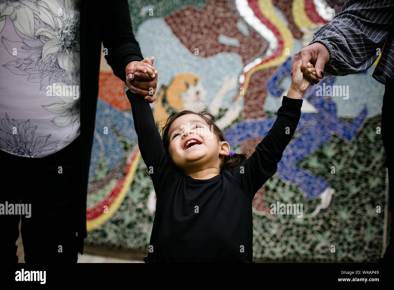 Little girl smiling and holding hands laughing in front of mural Stock Photo