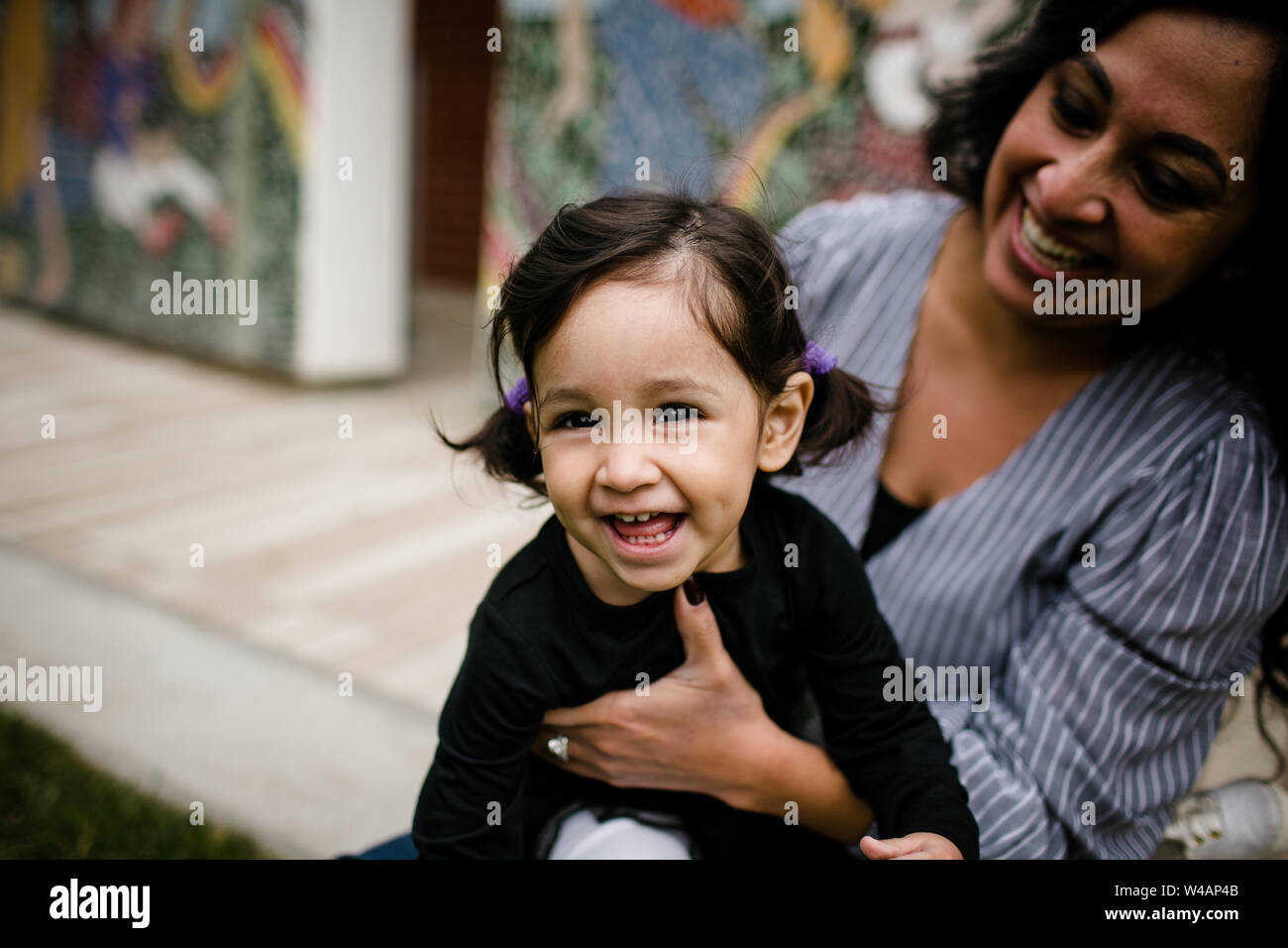 Daughter laughing as mom looks on in front of mural Stock Photo