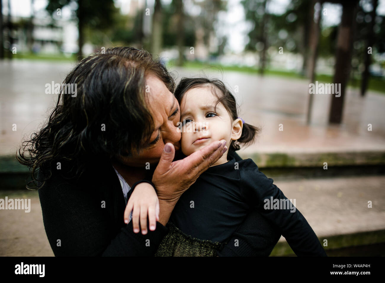 Grandmother kissing granddaughter while sitting in park Stock Photo