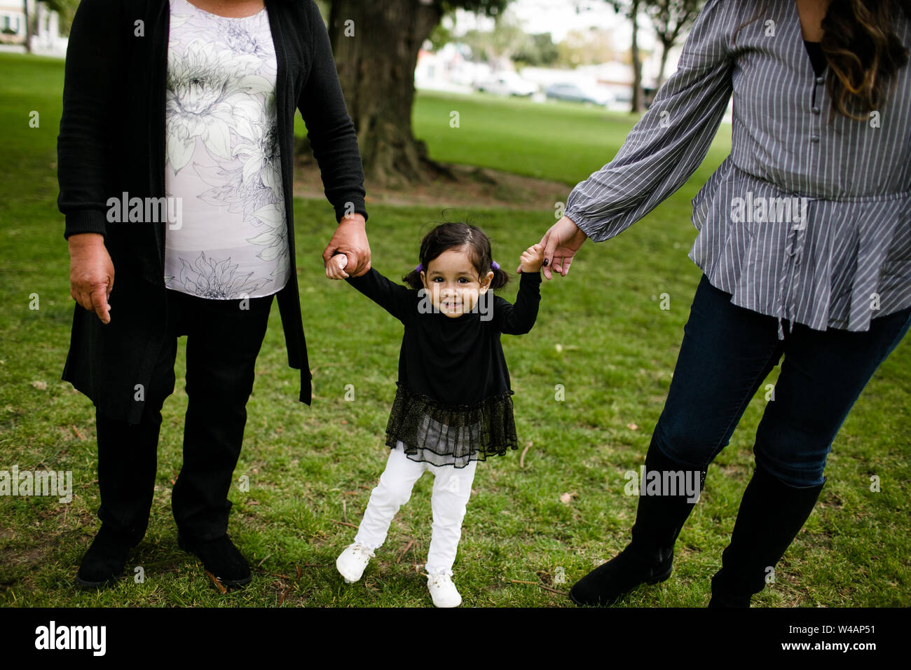 Little girl standing holding hands with mother and grandmother Stock Photo