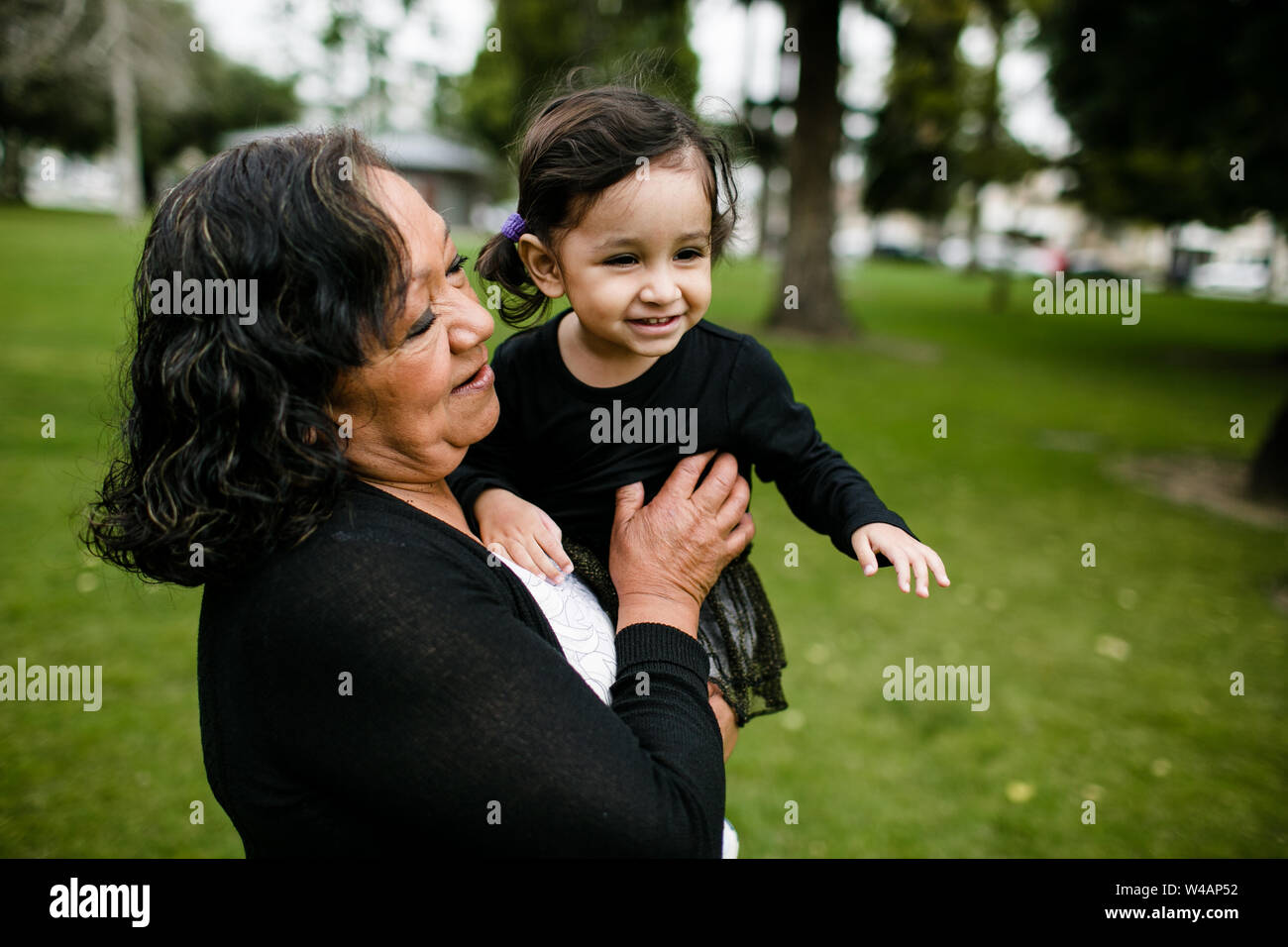 Grandmother & granddaughter smiling and hugging in park Stock Photo