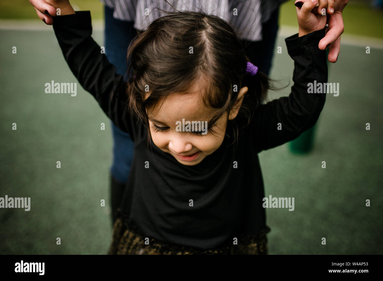 Mom holding daughter's hands while standing at park Stock Photo