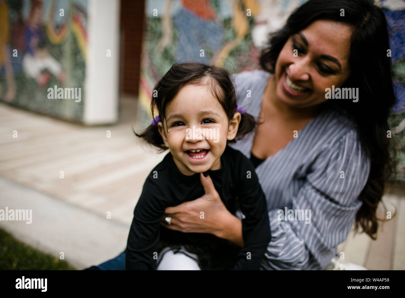 Daughter laughing as mother looks on in front of mural Stock Photo