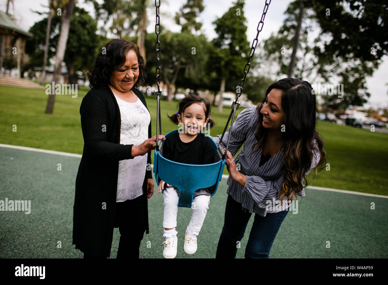Grandmother and mother pushing little girl laughing in swing Stock Photo