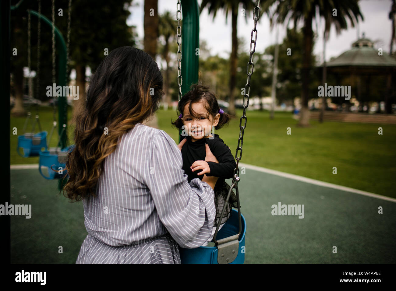 Mom putting daughter in swing at playground Stock Photo