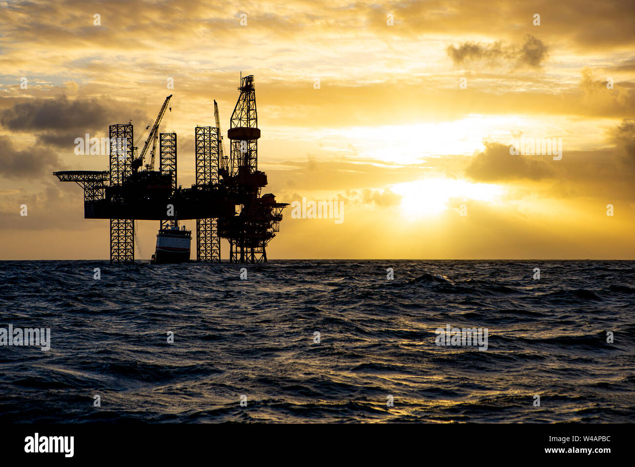 Offshore drilling platform during sunrise with work vessel Stock Photo