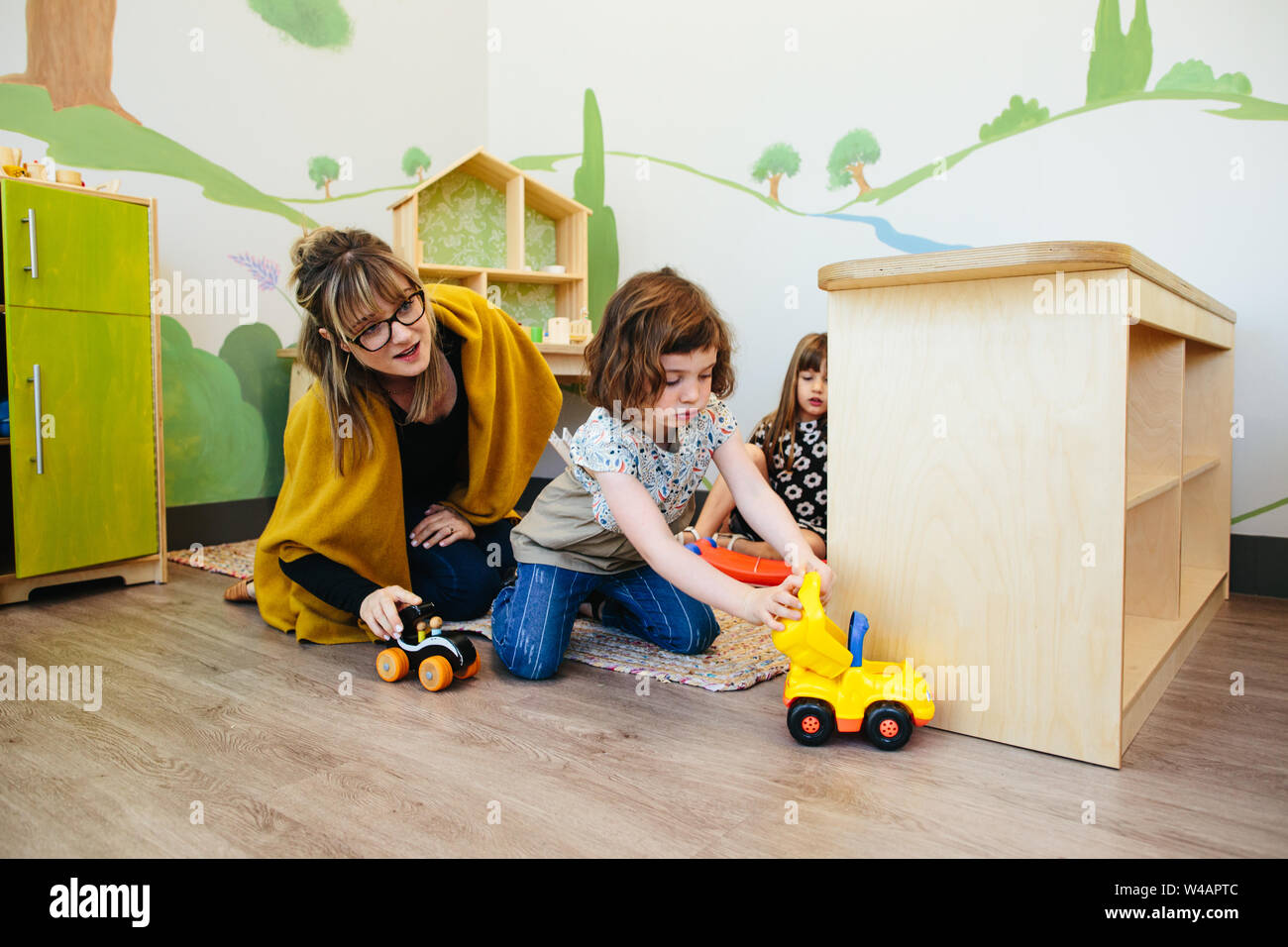 Teacher watches student as they play together with toy cars Stock Photo