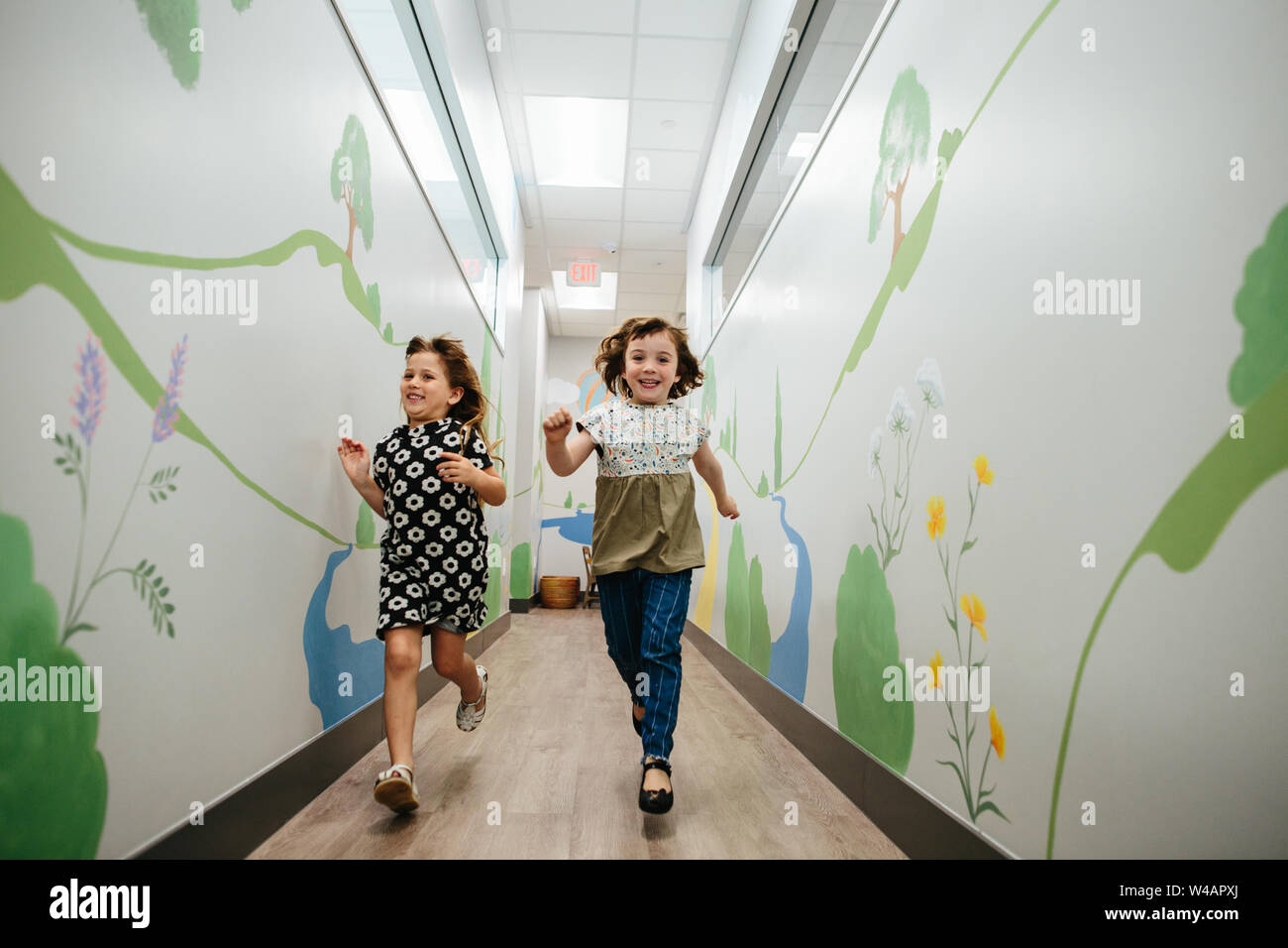 Two girls smile and run down a hallway in a school building Stock Photo