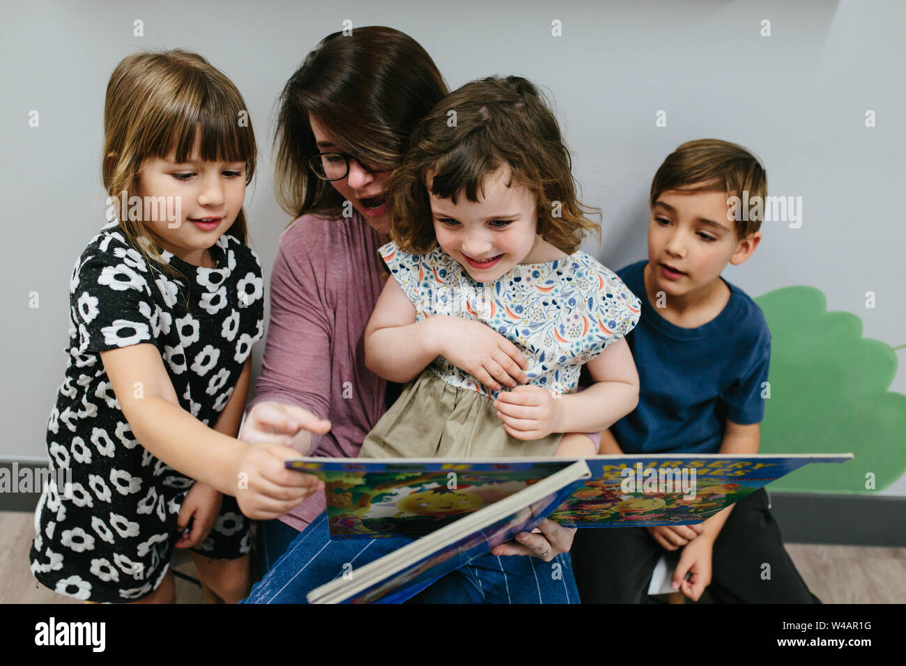 Girl sits on teacher's lap with two other students while reading book
