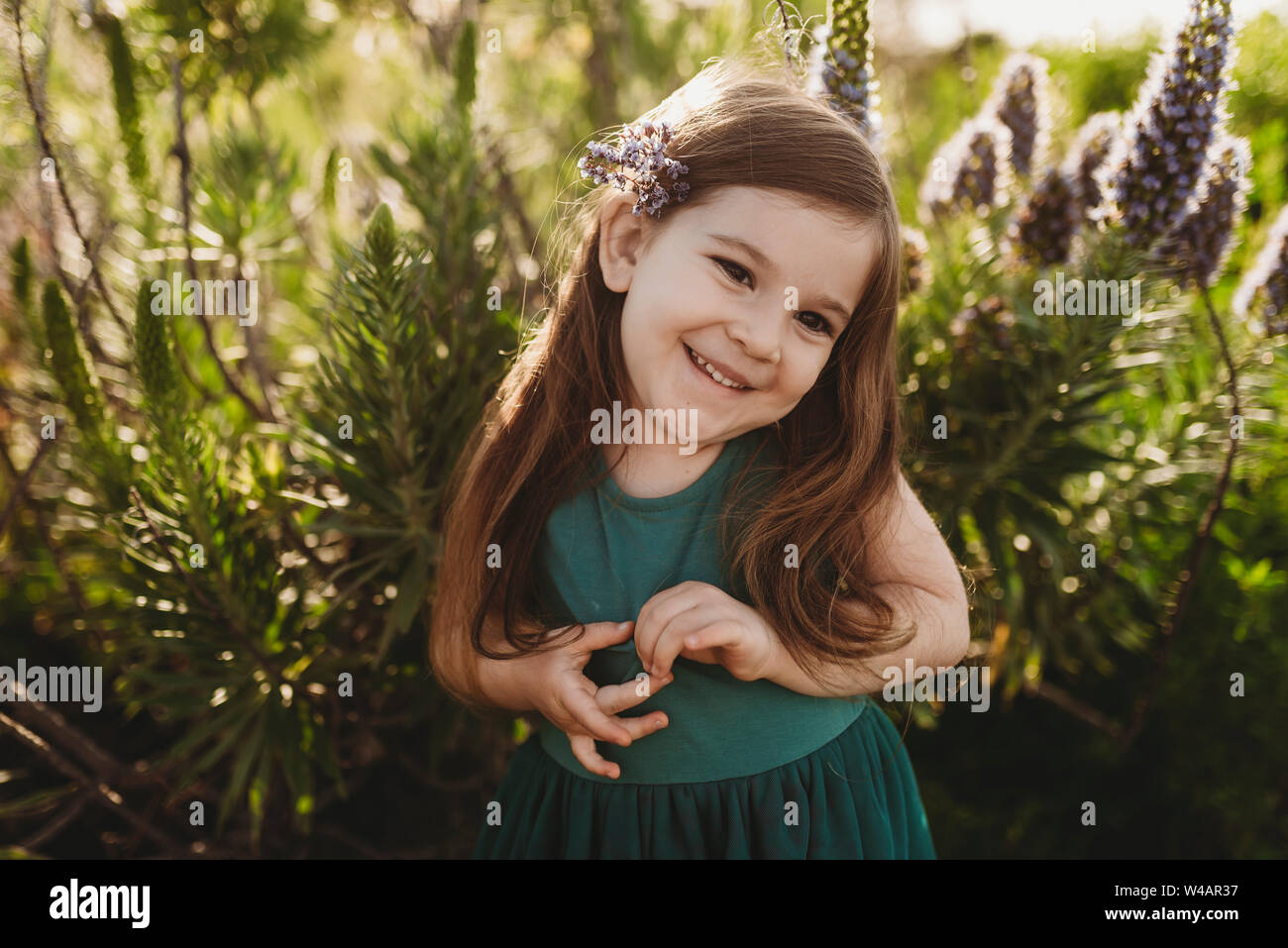 Portrait of little girl with flowers in her hair smiling in meadow ...