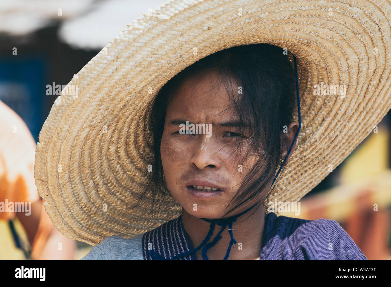 Indein, Myanmar - March 2019: portrait of a young Burmese woman in a big straw hat and tanaka on her face Stock Photo