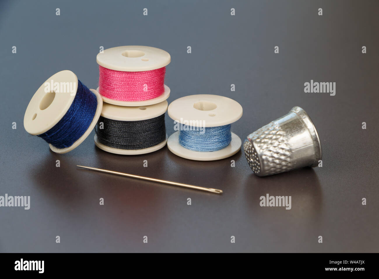 Blue, pink and gray reels of thread for sewing, needle and thimble Stock Photo