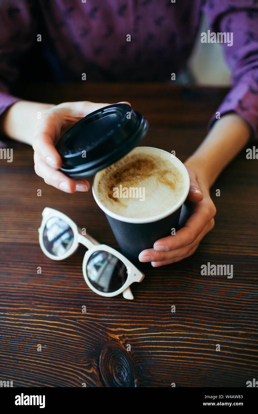 Female hands with a cup of cappuccino with thick foam in black takeaway paper cup. Stock Photo