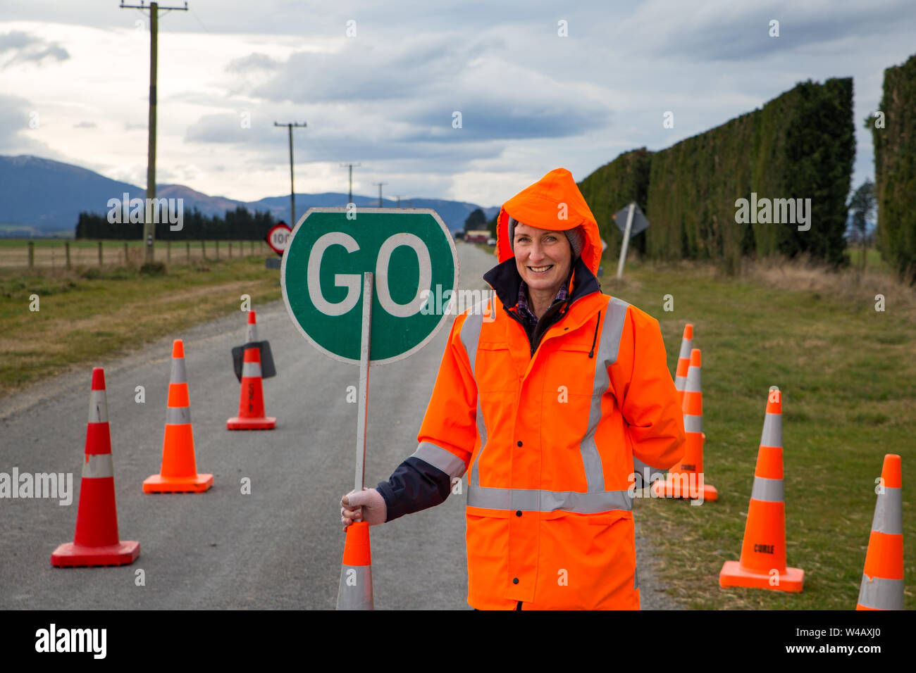 A female on a road crew operates a road sign and traffic cones at a hazard area on a rural country road in New Zealand Stock Photo