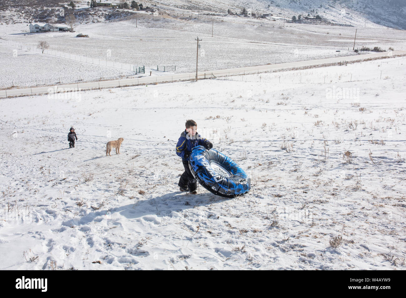 Boys and dog walking up sledding hill carrying snow tube Stock Photo