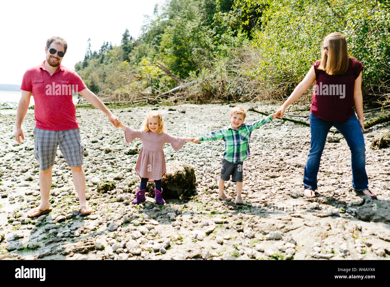 Straight on view of a family of four holding hands on a rocky beach Stock Photo
