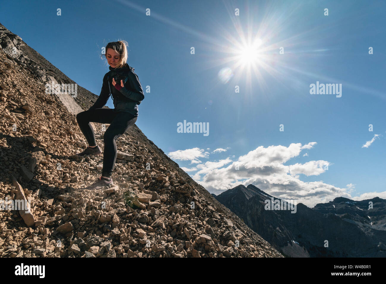 Female Trail Runner Scrambles Down Yamnuska Mountain Stock Photo