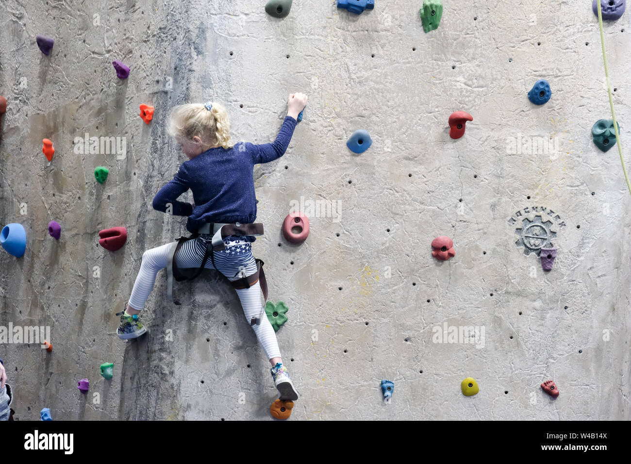 young girl climbing rock wall at indoor rock climbing gym Stock Photo
