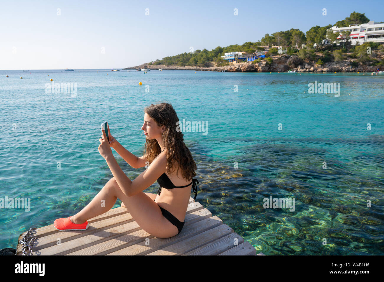 Ibiza girl taking smartphone photos at Portinatx beach  pier in Balearic Islands Stock Photo