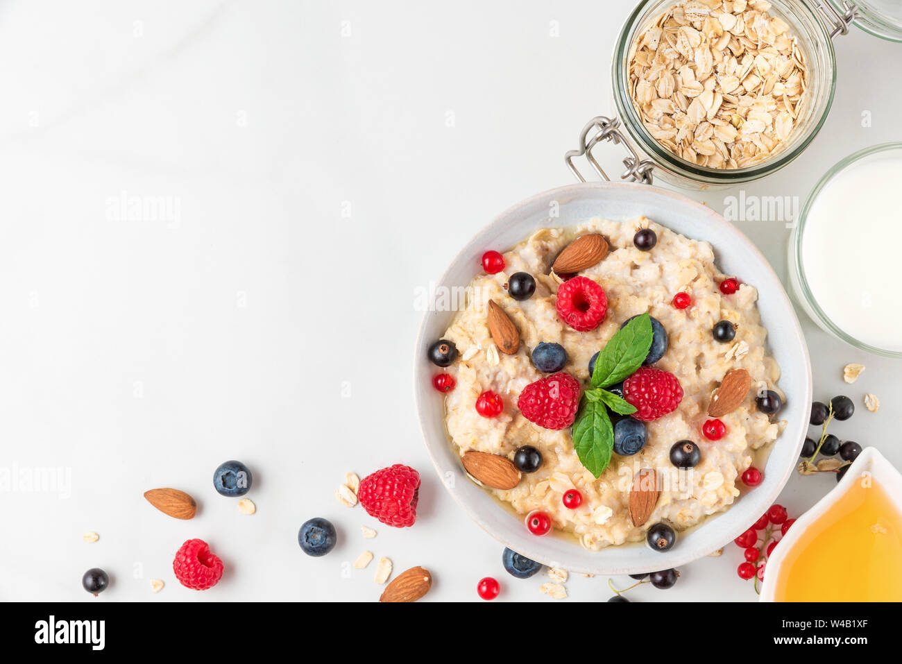 oatmeal porridge with fresh berries, nuts, honey and mint in a bowl for healthy diet breakfast. top view with copy space Stock Photo
