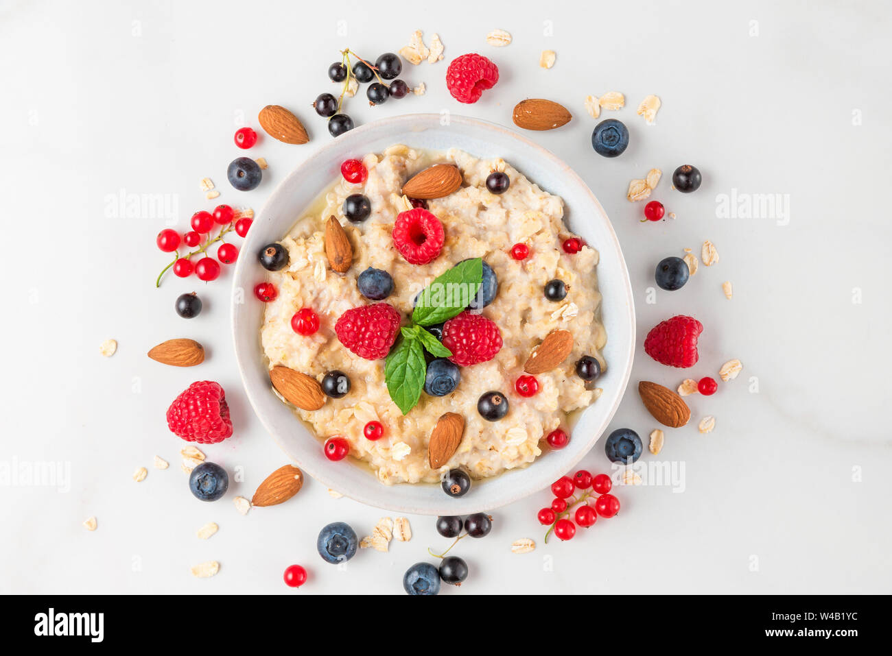 bowl of oatmeal porridge with fresh berries, nuts and mint for healthy diet breakfast on white marble table. top view Stock Photo