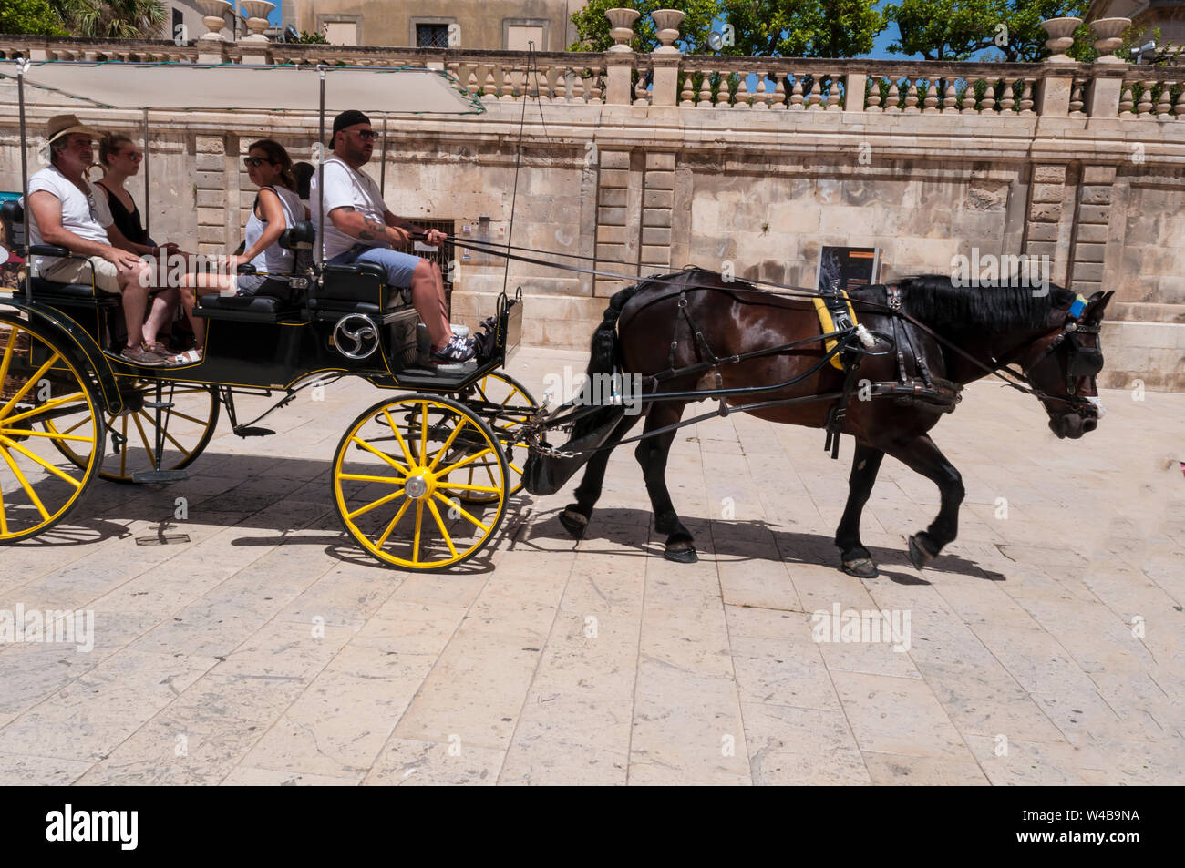 Visitors in a horse carriage shielded from the sun in the historic district of Ortegia, Siracusa, Sicily, Italy Stock Photo