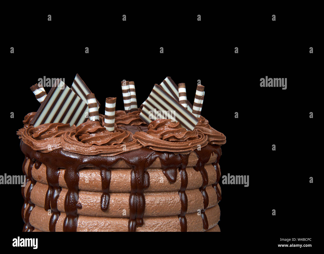 Close up on the top half of a chocolate cake with chocolate ganache dripping down the sides and candy garnish on top, isolated on black background. Stock Photo