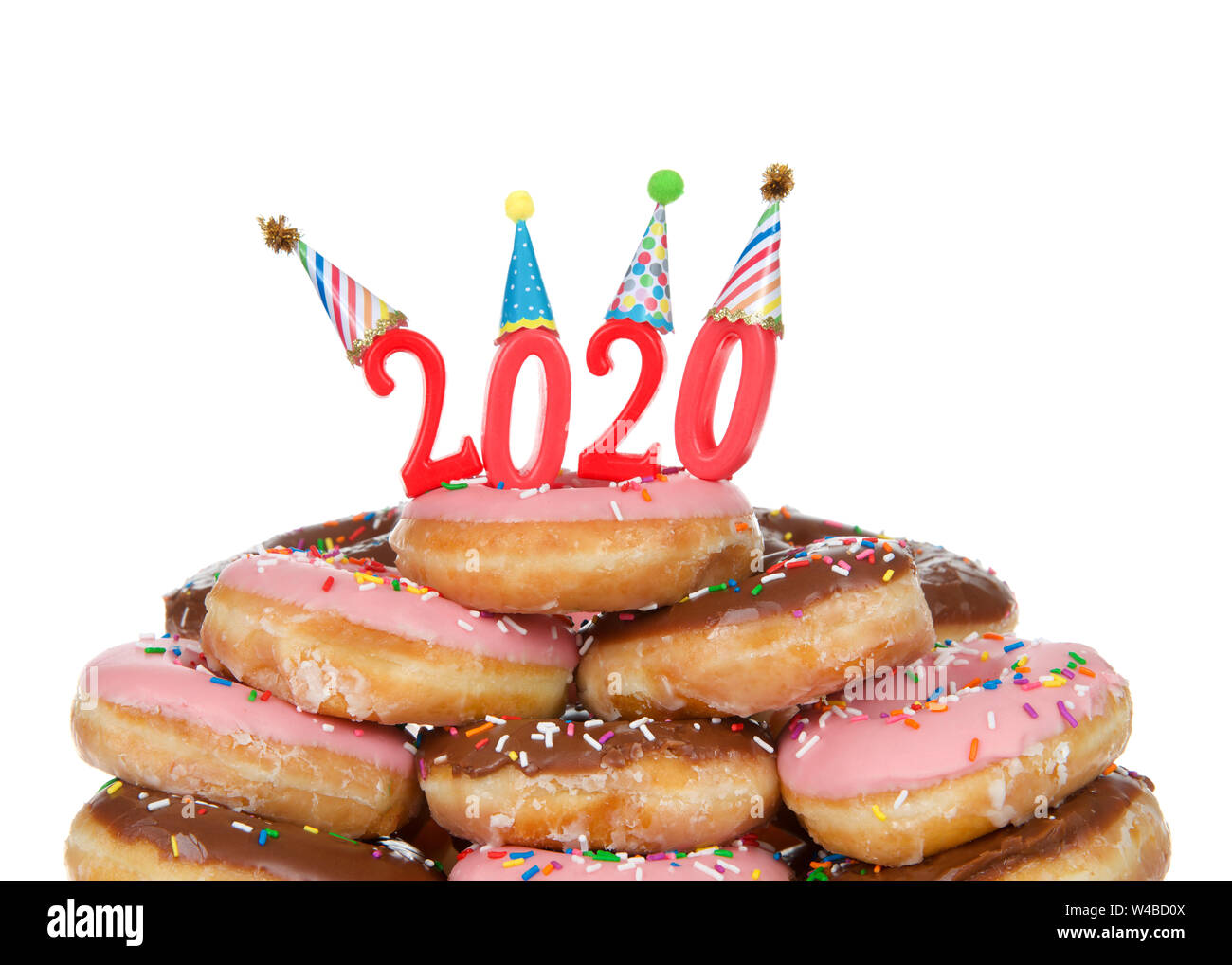 Variety of glazed donuts stacked with Happy 2020 candles wearing party hats, isolated on white. Happy New Year theme. Stock Photo