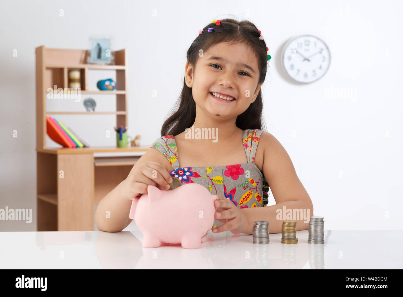 Girl inserting a coin into a piggy bank and smiling Stock Photo - Alamy