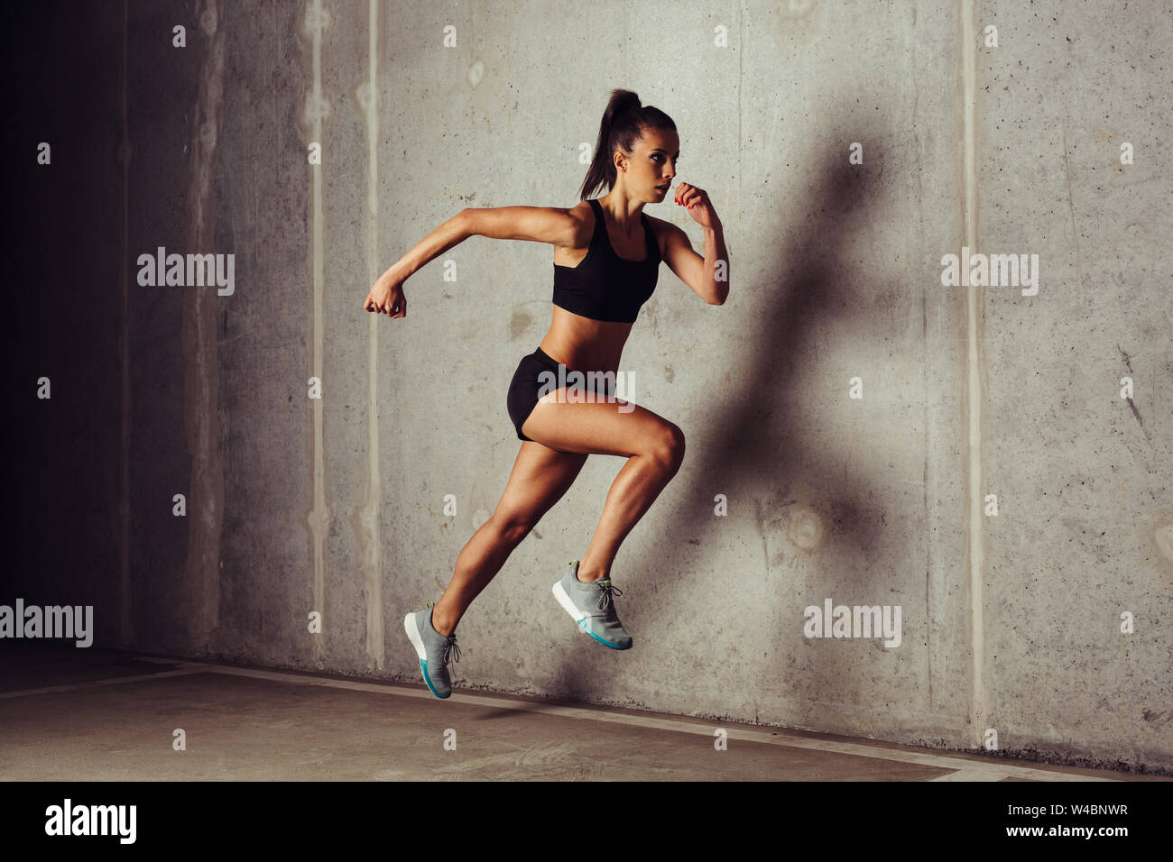 Slim attractive sportswoman running  against a concrete background Stock Photo