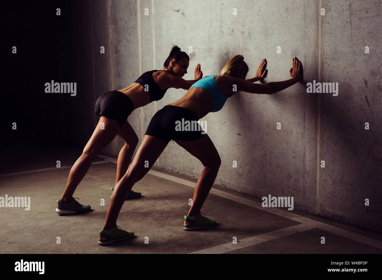 Two female athletes stretching against a concrete wall Stock Photo