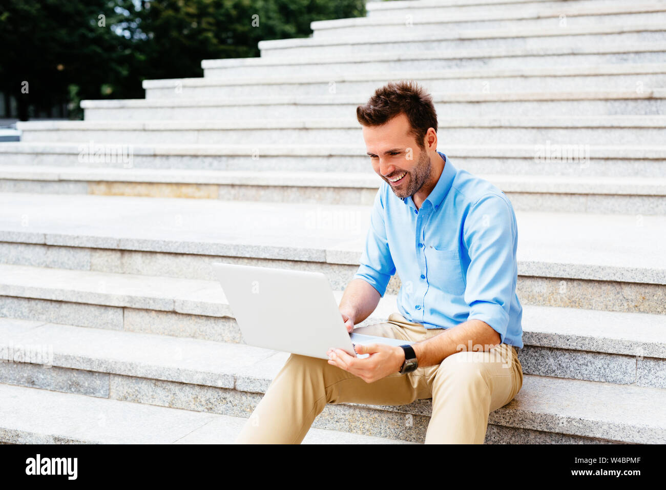 Handsome student sitting on stone stairs and using a laptop Stock Photo