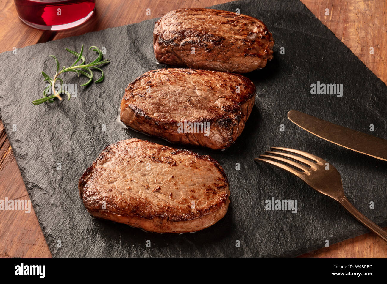 Sirloin beef steaks with rosemary and red wine on a black slate plate