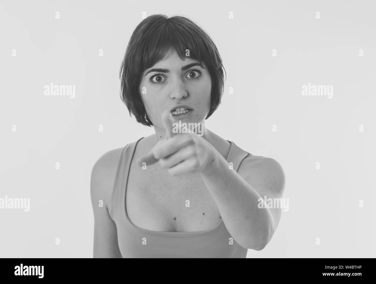 Black and white portrait of young attractive frustrated caucasian woman with angry face. Looking mad and crazy shouting and pointing at the camera. Co Stock Photo