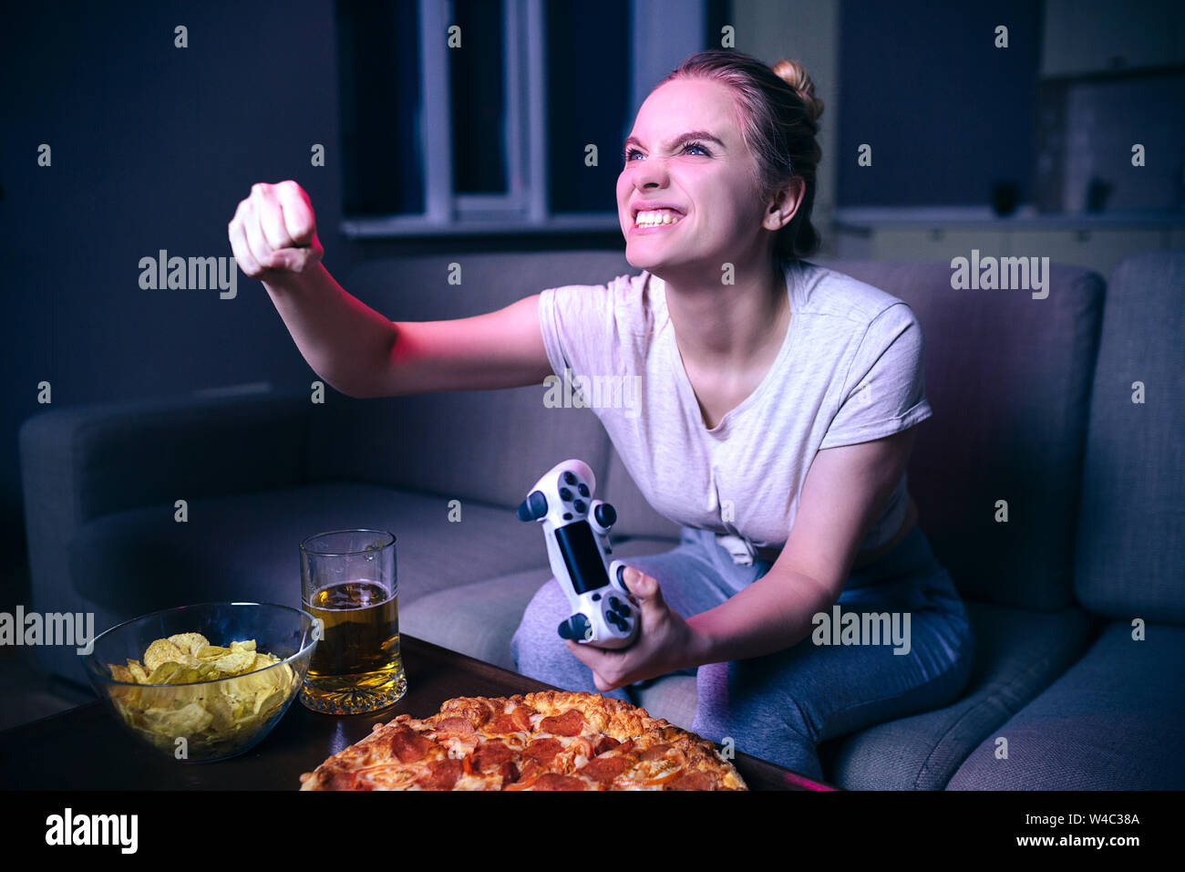 Young woman playing game at night. Angry cheering model hold hand in fist.  Gamepad. Junk food on table. Emotional intence woman Stock Photo - Alamy