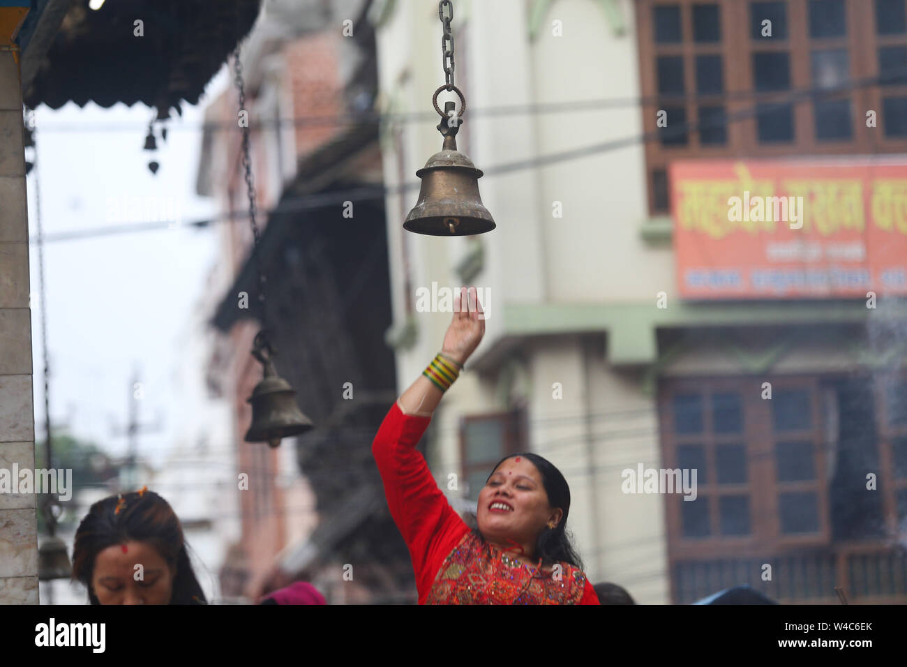 Kathmandu, Nepal. 22nd July, 2019. A woman seen trying to reach a bell hanging at the Shiva temple during a Shrawan Sombar festival.Shrawan month is considered as the holiest month of the year and each Somvar (Monday) of this month is known as Shrawan Somvar, during which devotees fast and worship Lord Shiva to pray for happiness for their families. Credit: SOPA Images Limited/Alamy Live News Stock Photo