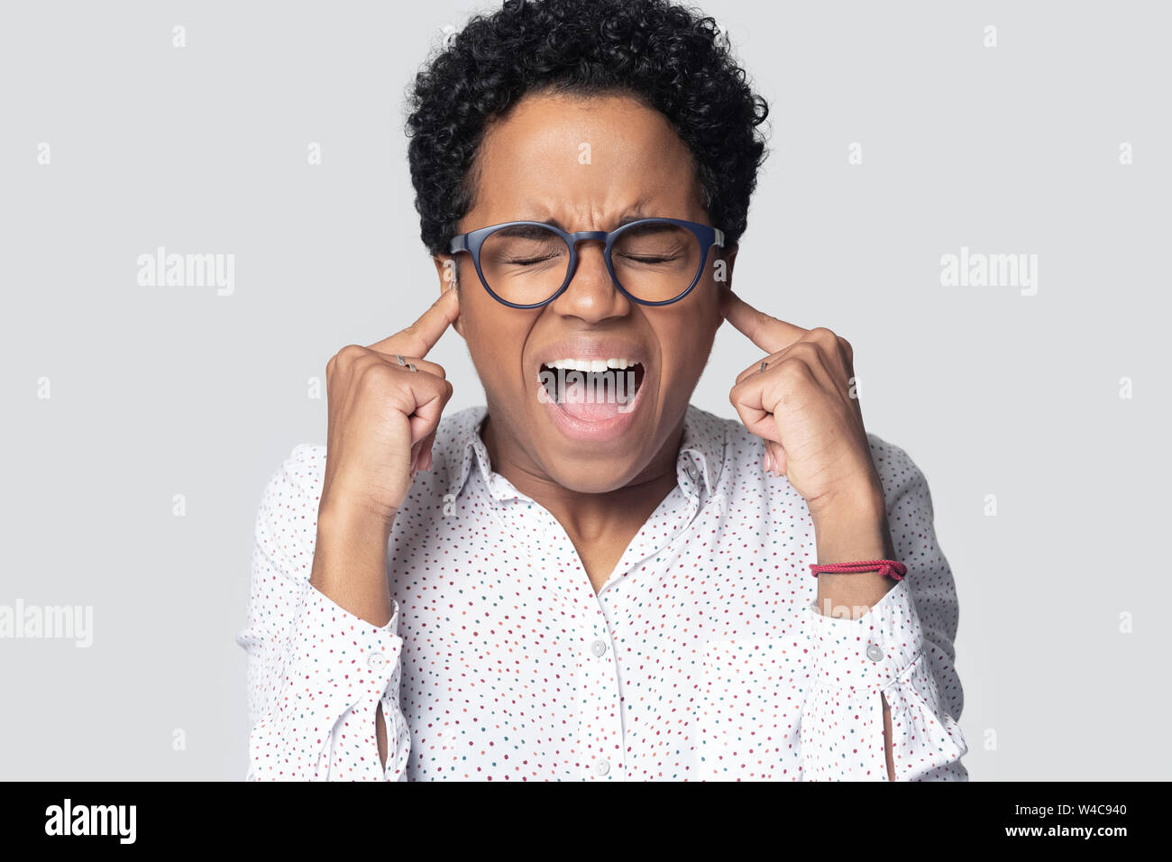 Stressed african American girl plug ears shout avoiding loud noise Stock Photo