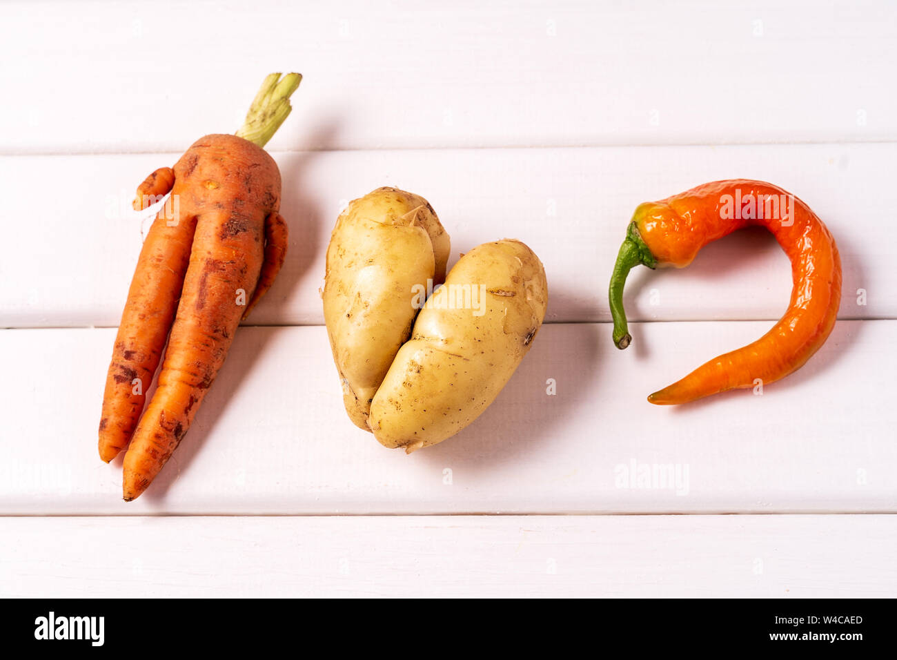 Flat lay Some ugly curved bent carrot, pepper and potato on white wooden background. Stock Photo