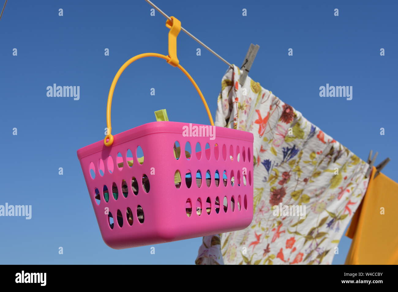 laundry hanging out to dry outdoors on a hot sunny, day. Close up, detail of pink peg basket, shirts and clothes pegs against blue sky background pegh Stock Photo