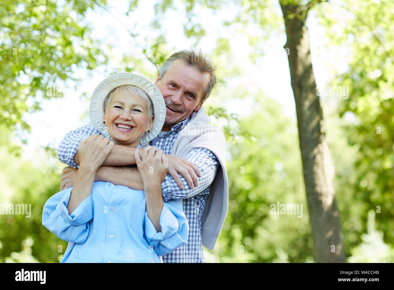 Portrait of happy senior couple embracing and looking at camera while enjoying walk in Summer park, copy space Stock Photo