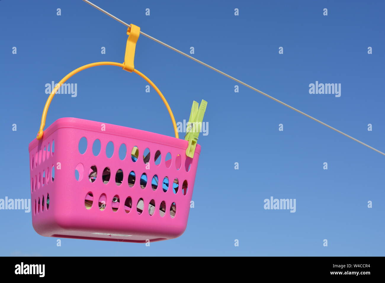 Laundry day. Pink peg basket hanging on the line against blue sky background with copy space. Stock Photo