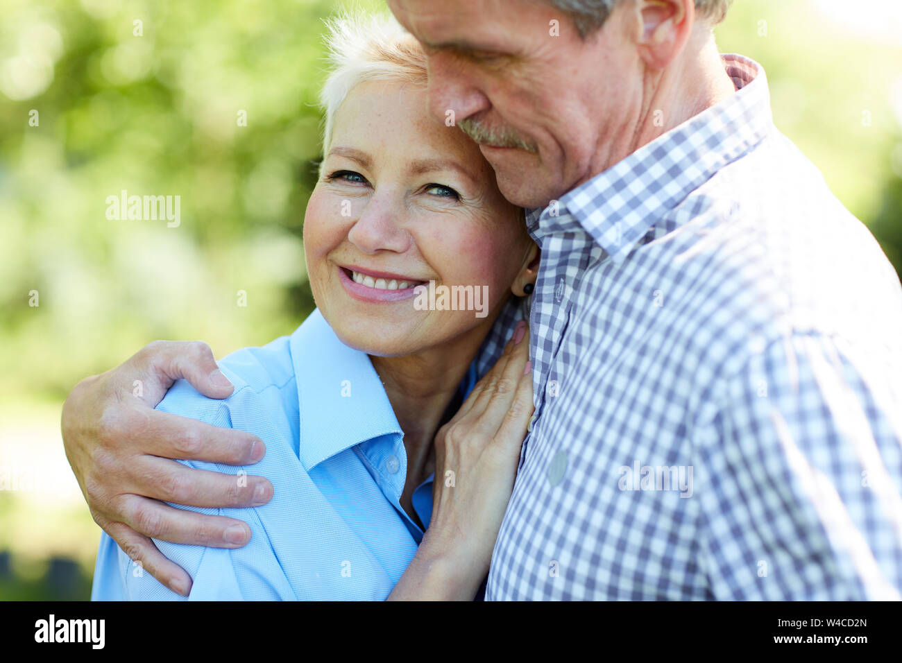 Waist up portrait of happy senior couple embracing with love while enjoying walk in Summer park Stock Photo