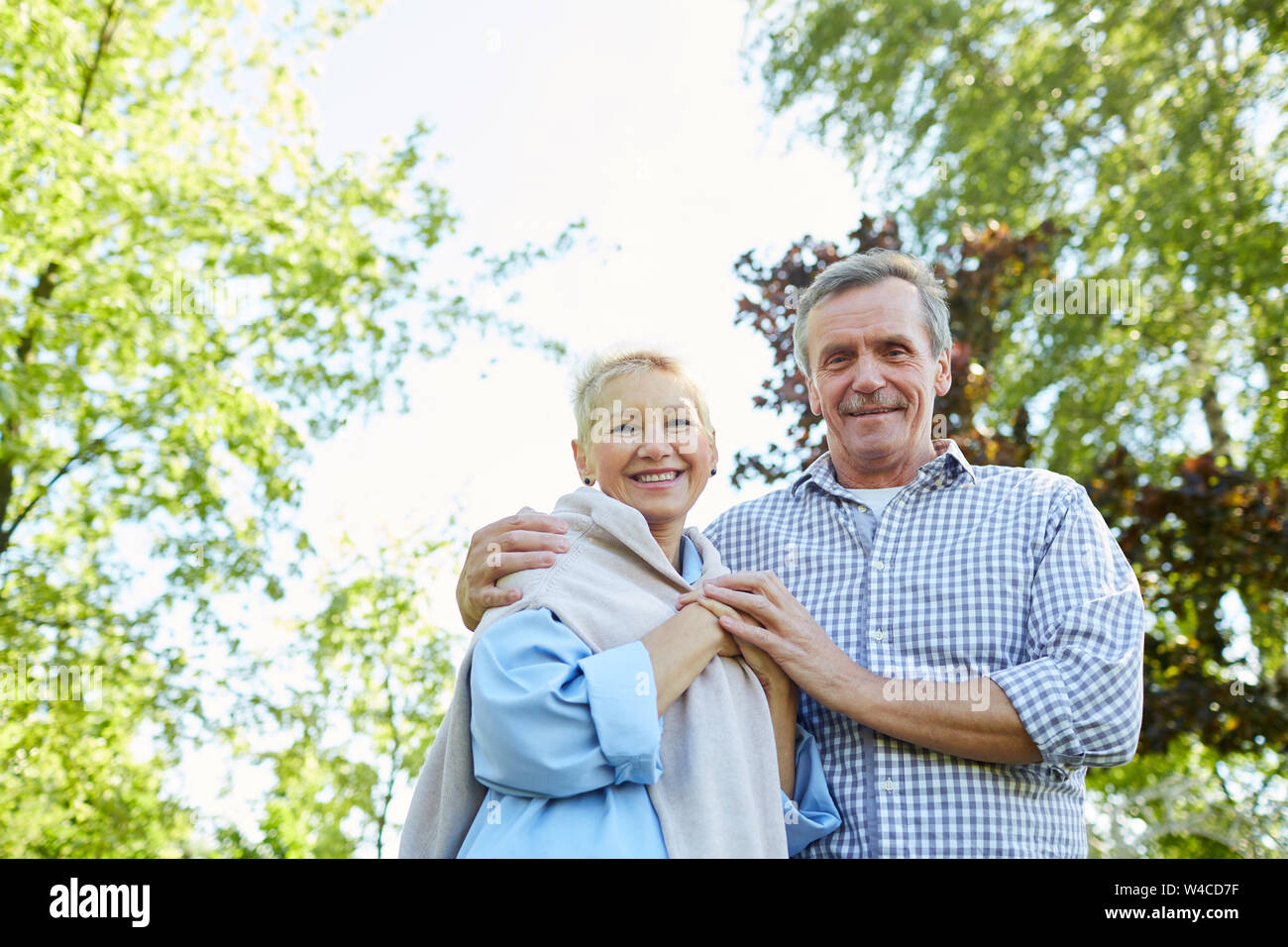 Low angle portrait of happy senior couple looking at camera and smiling while walking in Summer park, copy space Stock Photo