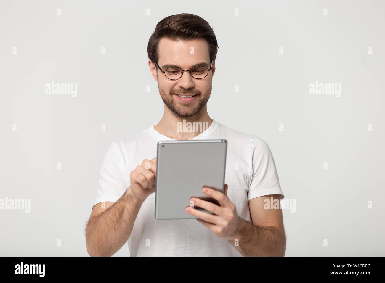 Millennial guy in glasses using tablet isolated on grey background Stock Photo