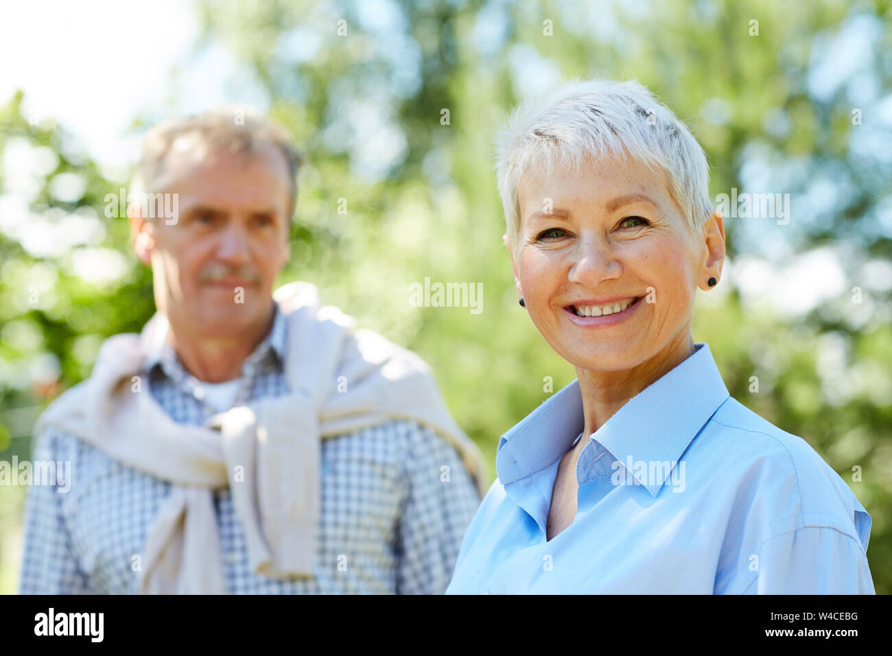Portrait of contemporary senior woman smiling at camera with loving husband in background, copy space Stock Photo