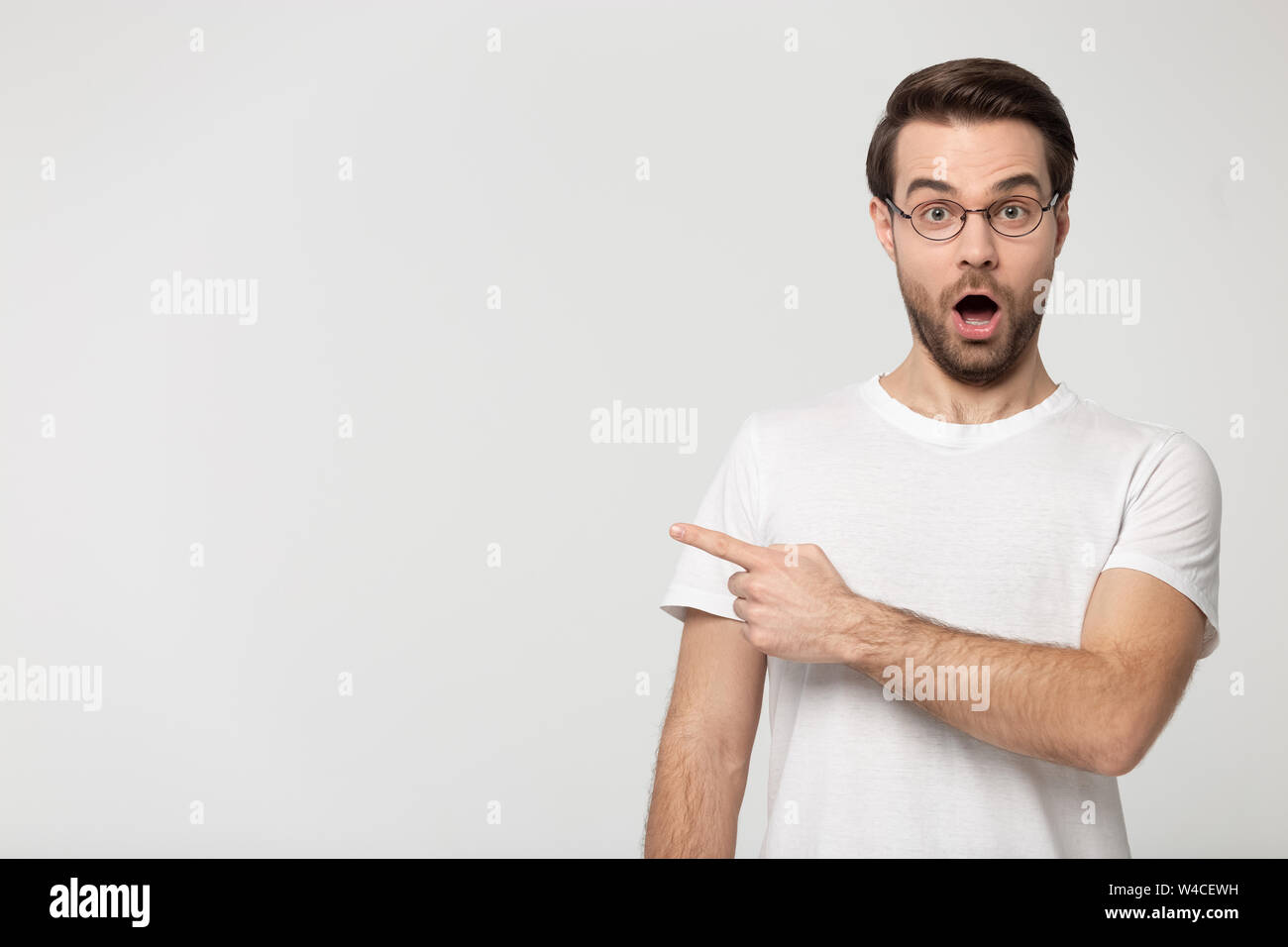 Surprised young man wearing glasses pointing finger aside at copyspace Stock Photo