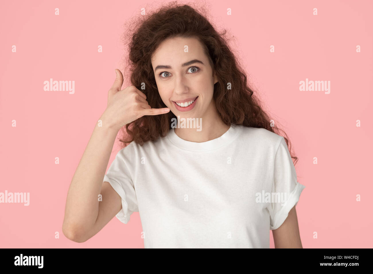 Smiling woman showing call me gesture with fingers studio shot Stock Photo