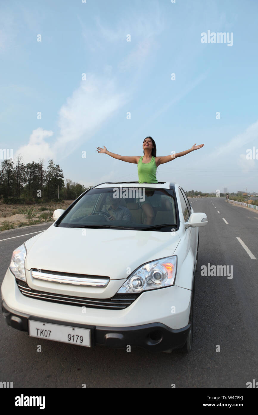 Man driving and woman standing in car sun roof in road Stock Photo