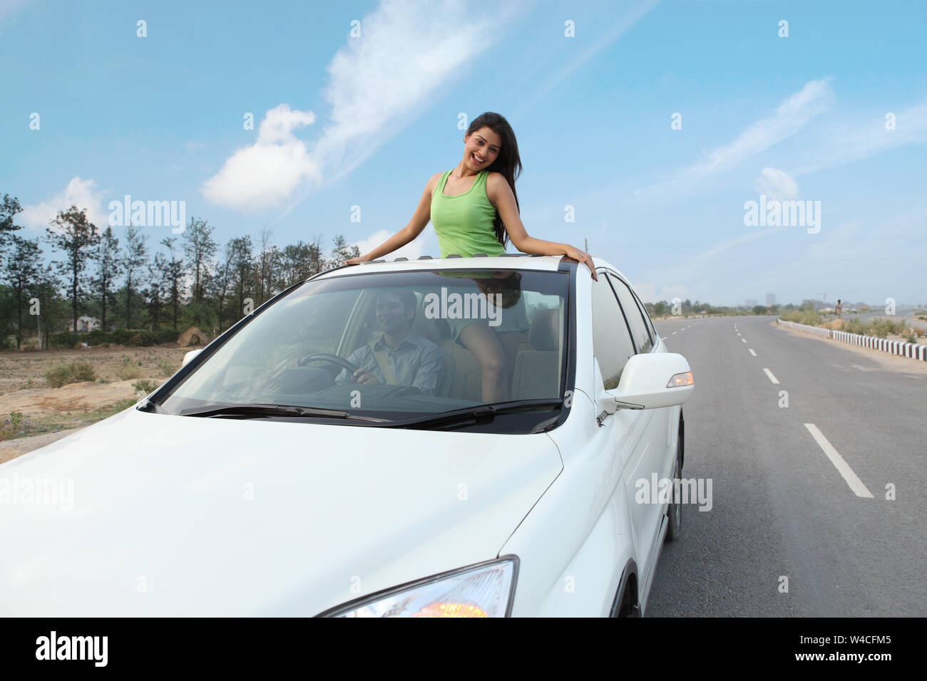 Man driving and woman standing in car sun roof in road Stock Photo